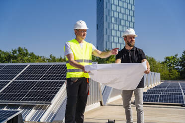 Zwei Techniker, die auf dem Dach eines mit Solarzellen bestückten Firmengebäudes Strategien entwickeln - DIGF20307