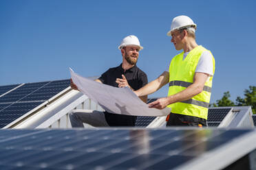 Zwei Techniker, die auf dem Dach eines mit Sonnenkollektoren ausgestatteten Firmengebäudes Strategien entwickeln - DIGF20312
