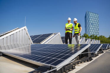 Zwei Techniker arbeiten mit einem Tablet-PC auf dem Dach eines mit Solarzellen ausgestatteten Firmengebäudes - DIGF20315