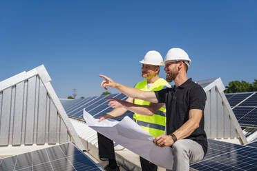 Zwei Solarteure besprechen den Installationsplan auf dem Dach eines Firmengebäudes mit Solarzellen. - DIGF20318