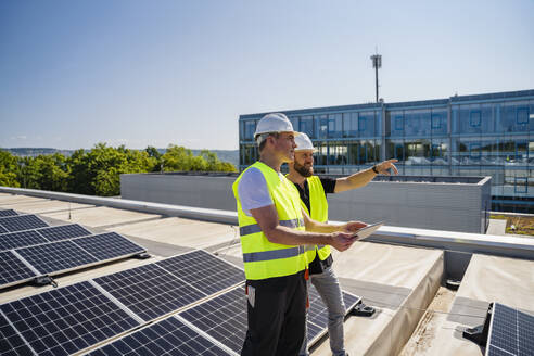 Two technicians on a company building's roof use a tablet PC to monitor solar panels - DIGF20325