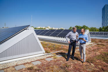 Zwei Führungskräfte besprechen Geschäftsstrategien, während sie die Aussicht auf ihr umweltfreundliches, mit Solarzellen bestücktes Bürodach genießen - DIGF20329