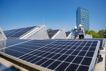 Zwei Führungskräfte diskutieren über nachhaltige Energielösungen auf dem Dach ihres Unternehmens, das mit Sonnenkollektoren und Schutzhelmen geschmückt ist - DIGF20339