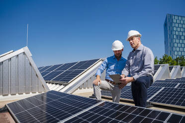 Zwei leitende Angestellte mit Schutzhelmen diskutieren auf dem Dach eines solarbetriebenen Firmengebäudes - DIGF20342