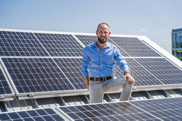 A cheerful businessman stands surrounded by solar panels, showcasing his commitment to sustainable energy - DIGF20354