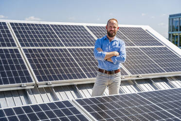 Ein selbstbewusster Geschäftsmann steht selbstsicher inmitten eines Feldes von Solarmodulen - DIGF20355
