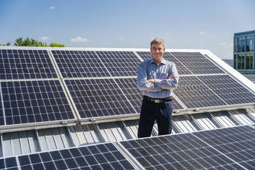 A self-assured businessman stands proudly surrounded by rows of gleaming solar panels - DIGF20358