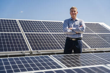 Eine selbstbewusste männliche Führungskraft steht stolz inmitten eines Feldes von Solarzellen - DIGF20360