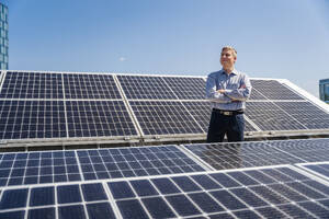 Eine selbstbewusste männliche Führungskraft posiert selbstsicher inmitten eines Feldes von Solarzellen - DIGF20361