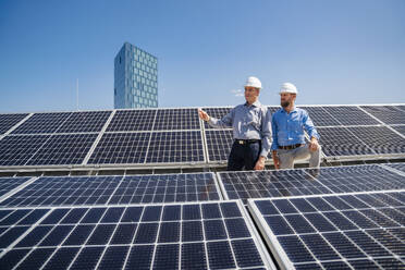 Zwei Geschäftsleute mit Schutzhelmen diskutieren über die Installation von Solarzellen - DIGF20364
