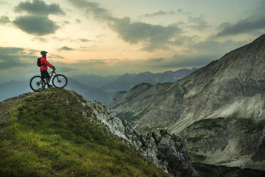 Biker with bicycle on top of mountain under cloudy sky - HHF05896