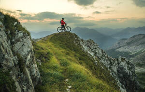 Aktiver Mann mit Fahrrad auf einem Berg bei Sonnenuntergang - HHF05897