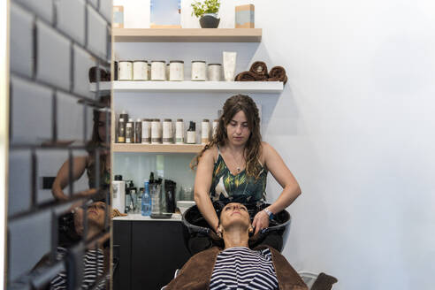 Junge Friseurin wäscht einer Frau die Haare im Salon - PBTF00128