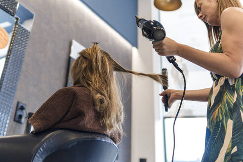 Friseurin kämmt das Haar eines Kunden mit einer Haarbürste im Salon - PBTF00129