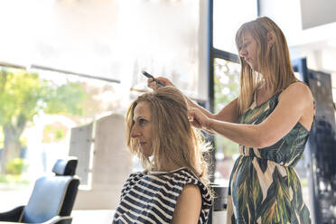 Hairdresser styling woman's hair at salon - PBTF00131