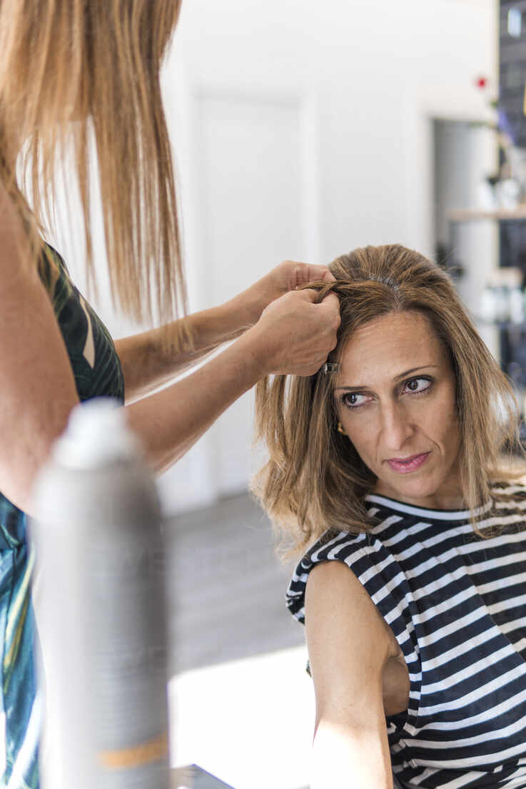 Crop Stylist mit Trockner und Kamm und machen Frisur zu attraktiven Frau im  Friseursalon, lizenzfreies Stockfoto