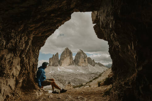 Italien, Männlicher Wanderer mit Blick auf die Drei Zinnen von Lavaredo vom Höhleneingang aus - FDF00392