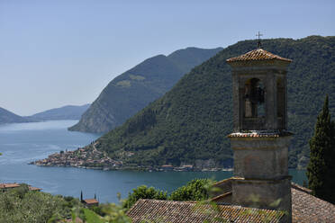 Italien, Lombardei, Iseosee umgeben von bewaldeten Bergen mit Glockenturm im Vordergrund - FDF00403