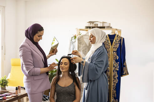 Lächelnde Visagisten bereiten die Braut für die Hochzeit in einer Boutique vor - JCCMF10676