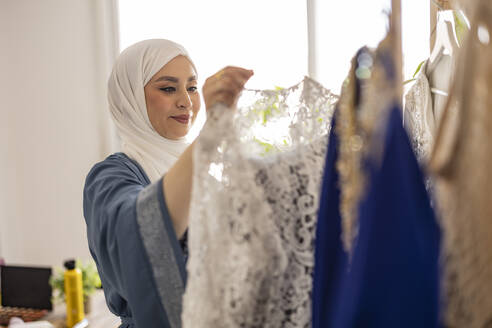 Lächelnde Modedesignerin bei der Auswahl des Hochzeitskleides - JCCMF10685