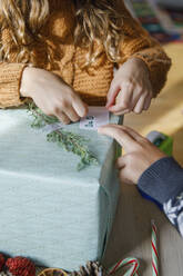 Boy with sister sticking note on Christmas present at home - IKF01151