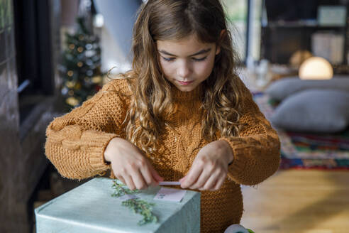Mädchen klebt Namensschild auf Weihnachtsgeschenk zu Hause - IKF01152