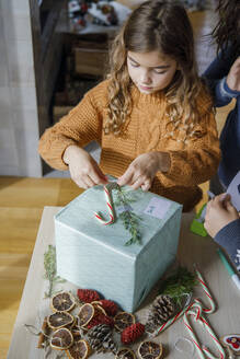 Girl decorating gift box with candy cane at home - IKF01153