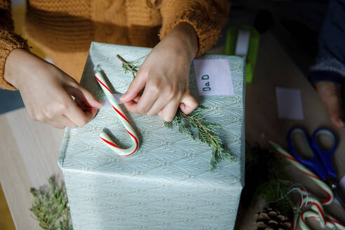 Girl sticking candy cane on gift box at home - IKF01155