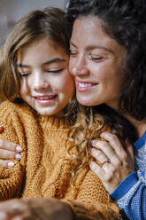 Smiling mother hugging daughter at home - IKF01158