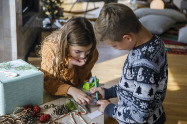 Schwester mit Bruder schreibt Notiz in der Nähe von Geschenk-Box zu Hause - IKF01163