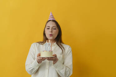 Frau bläst Kerze auf Geburtstagskuchen vor gelbem Hintergrund aus - OSF02008