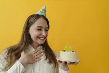 Lächelnde Frau starrt auf Geburtstagskuchen vor gelbem Hintergrund - OSF02011