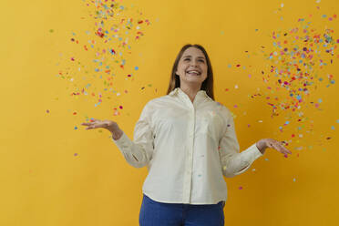 Smiling woman catching confetti standing against yellow background - OSF02013