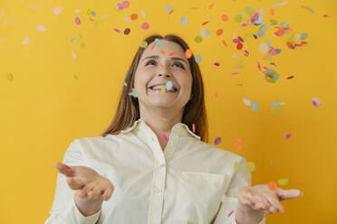 Happy woman catching confetti against yellow background - OSF02014