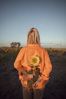 Frau hält Sonnenblume in einem Feld bei Sonnenuntergang - ADF00146