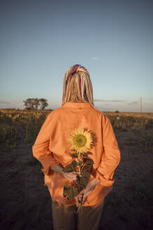 Woman holding sunflower in field at sunset - ADF00146