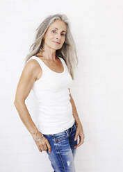 Smiling woman wearing jeans standing against white background - JBYF00240