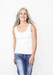 Smiling woman with gray hair standing against white background - JBYF00243