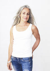 Mature woman wearing jeans standing against white background - JBYF00245