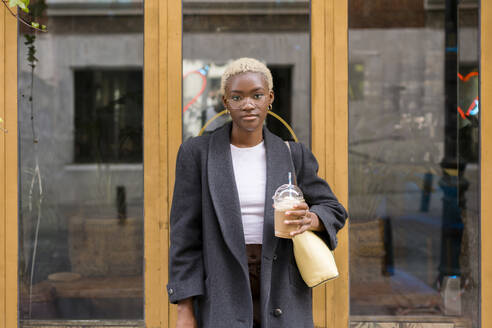 Geschäftsfrau mit kaltem Kaffee in der Hand und vor einer Glastür stehend - MMPF00825