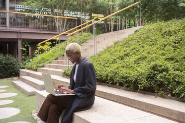 Smiling businesswoman using laptop in office park - MMPF00834