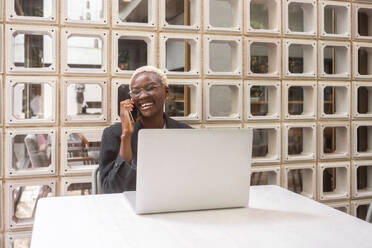 Lächelnde Geschäftsfrau, die in einem Straßencafé mit ihrem Smartphone telefoniert - MMPF00843