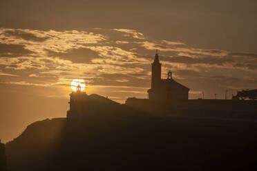 Sun aligned with the silhouette of the lighthouse and church of Luarca, Asturias, Spain, Europe - RHPLF27180