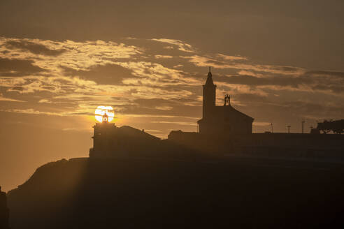 Sun aligned with the silhouette of the lighthouse and church of Luarca, Asturias, Spain, Europe - RHPLF27180