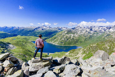One man looking at the alpine lake of Montespluga standing on rocks, Madesimo, Valle Spluga, Valtellina, Lombardy, Italy, Europe - RHPLF27287