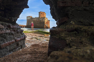 Blick von unten auf einen Mann, der vor der Burg Torre Astura steht, gesehen durch ein Loch in der Mauer, Provinz Rom, Tyrrhenisches Meer, Latium (Latium), Italien, Europa - RHPLF27293