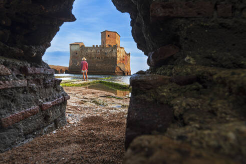Blick von unten auf einen Mann, der vor der Burg Torre Astura steht, gesehen durch ein Loch in der Mauer, Provinz Rom, Tyrrhenisches Meer, Latium (Latium), Italien, Europa - RHPLF27293