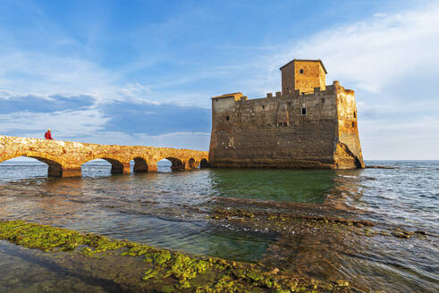 Mann auf der Brücke geht zum befestigten Schloss von Torre Astura im Wasser des Tyrrhenischen Meeres, das auf den Ruinen einer römischen Villa erbaut wurde, Sonnenuntergang, Provinz Rom, Latium (Lazio), Italien, Europa - RHPLF27295