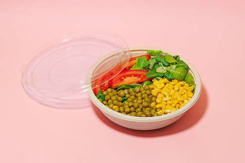 High angle of salad bowl with slices of tomato, spinach leaves, corn kernels and peas placed on pink surface - ADSF46661