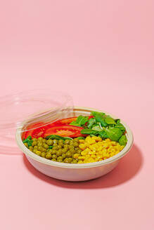 High angle of salad bowl with slices of tomato, spinach leaves, corn kernels and peas placed on pink surface - ADSF46662
